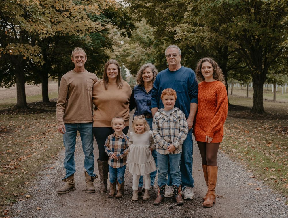 Extended family of eight poses together on a tree-lined path surrounded by colorful autumn foliage.