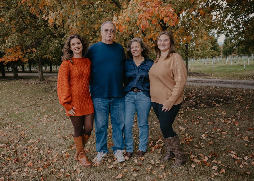 Family of four poses together in an autumn park surrounded by vibrant orange and red fall foliage.