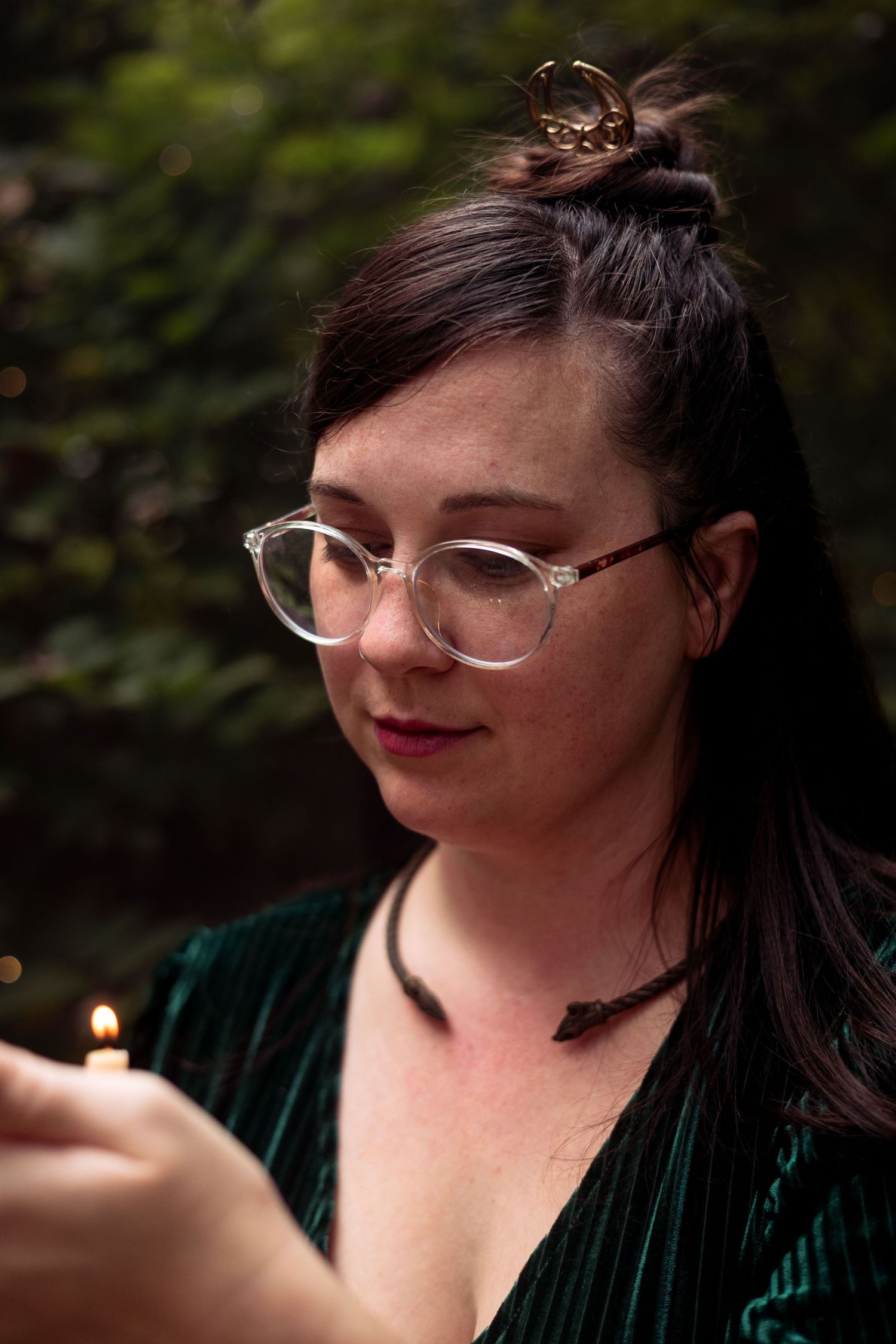 A woman in glasses blocks a candle flame from being blown out by the wind.