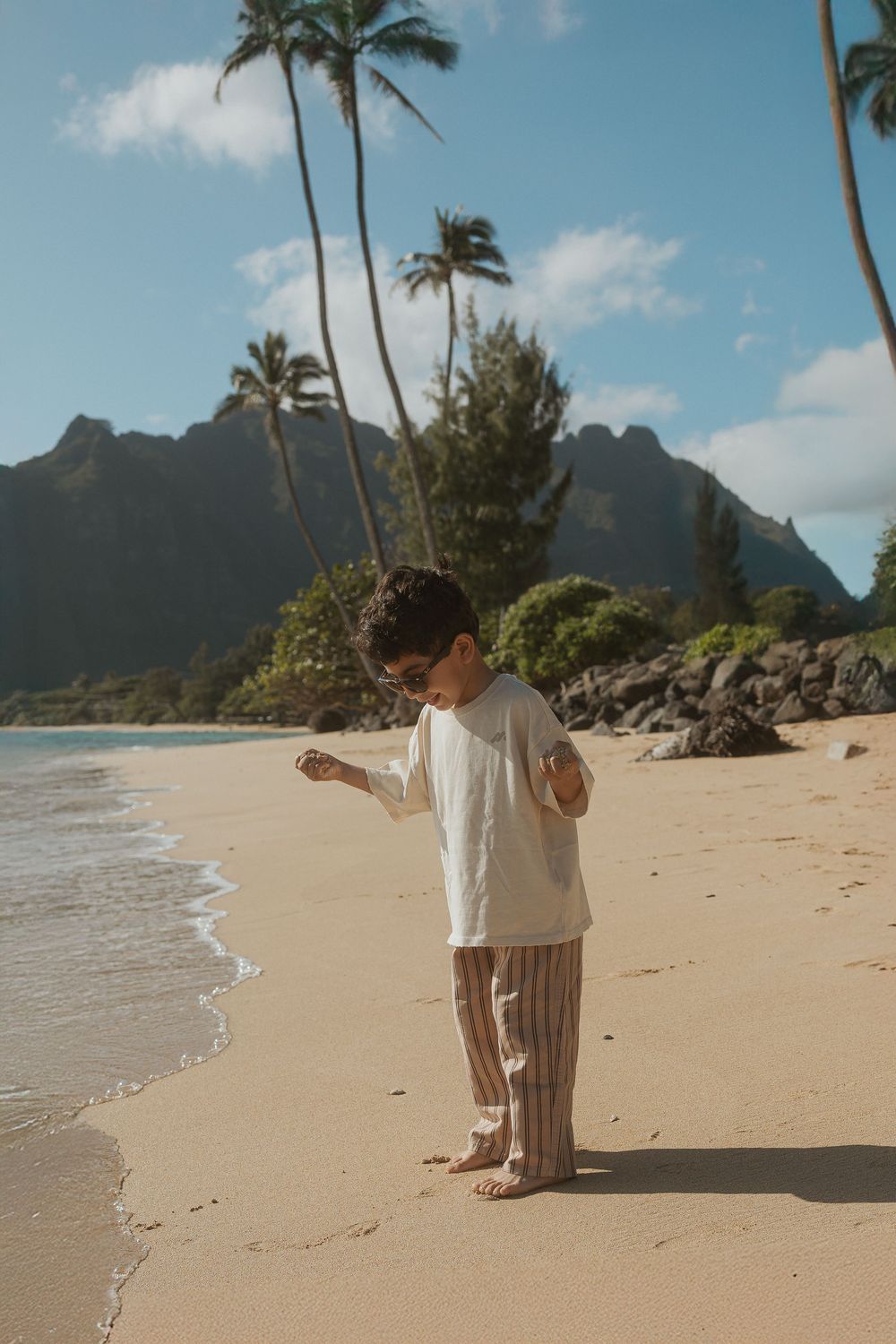 Four sequential photos show a serene beach scene with swaying palm trees, mountains, and someone walking along the shoreline.