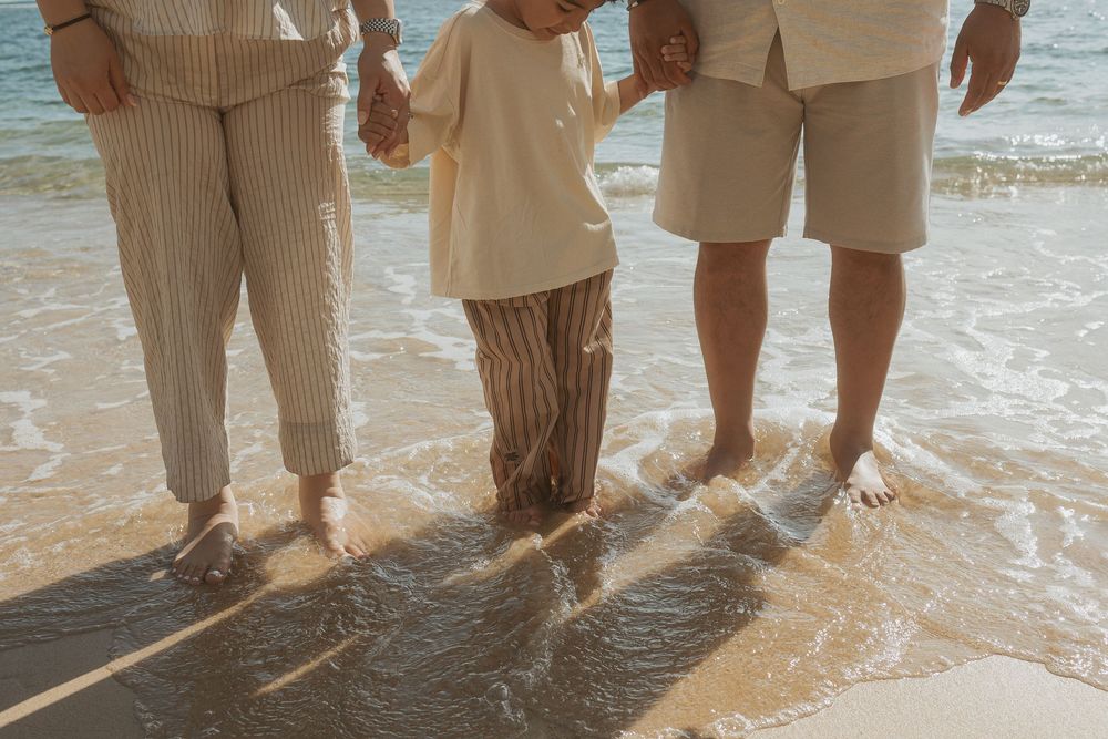 A group of feet and legs standing in the shallow ocean water as waves roll in at the beach.