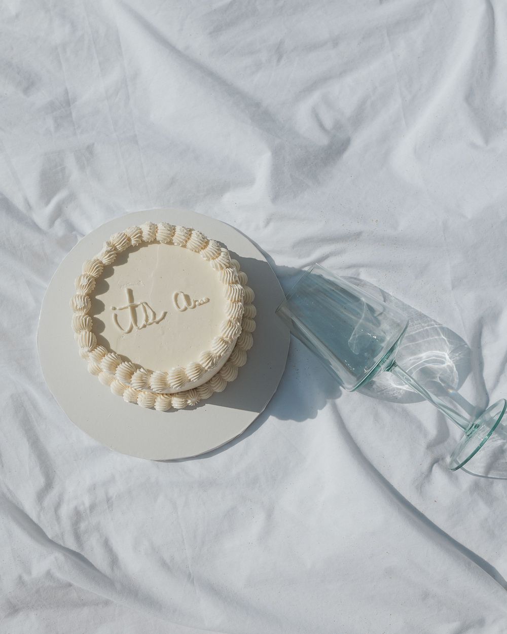 White ceramic cake plate with decorative piping details and glassware on a light textile background.