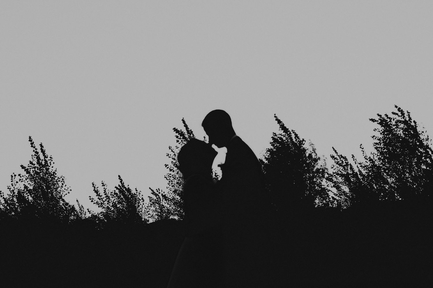 A romantic black and white wedding photograph showing a tender embrace in a natural outdoor setting.