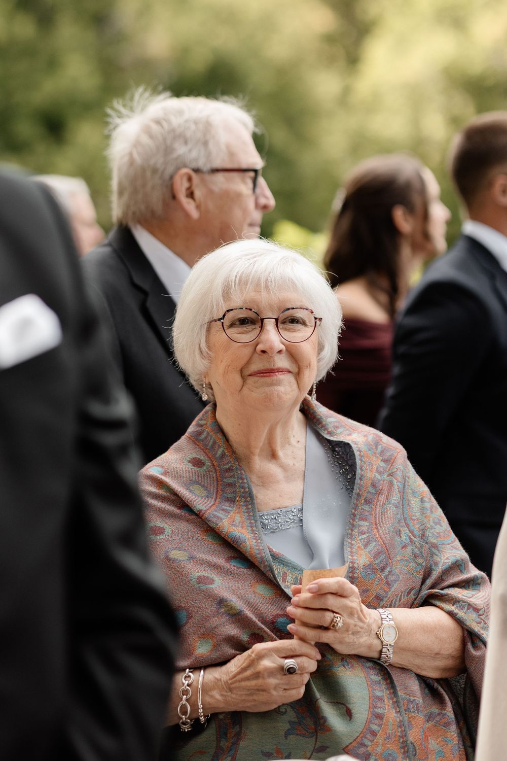 An elderly woman in a floral shawl and glasses smiles warmly in a series of candid outdoor photos.
