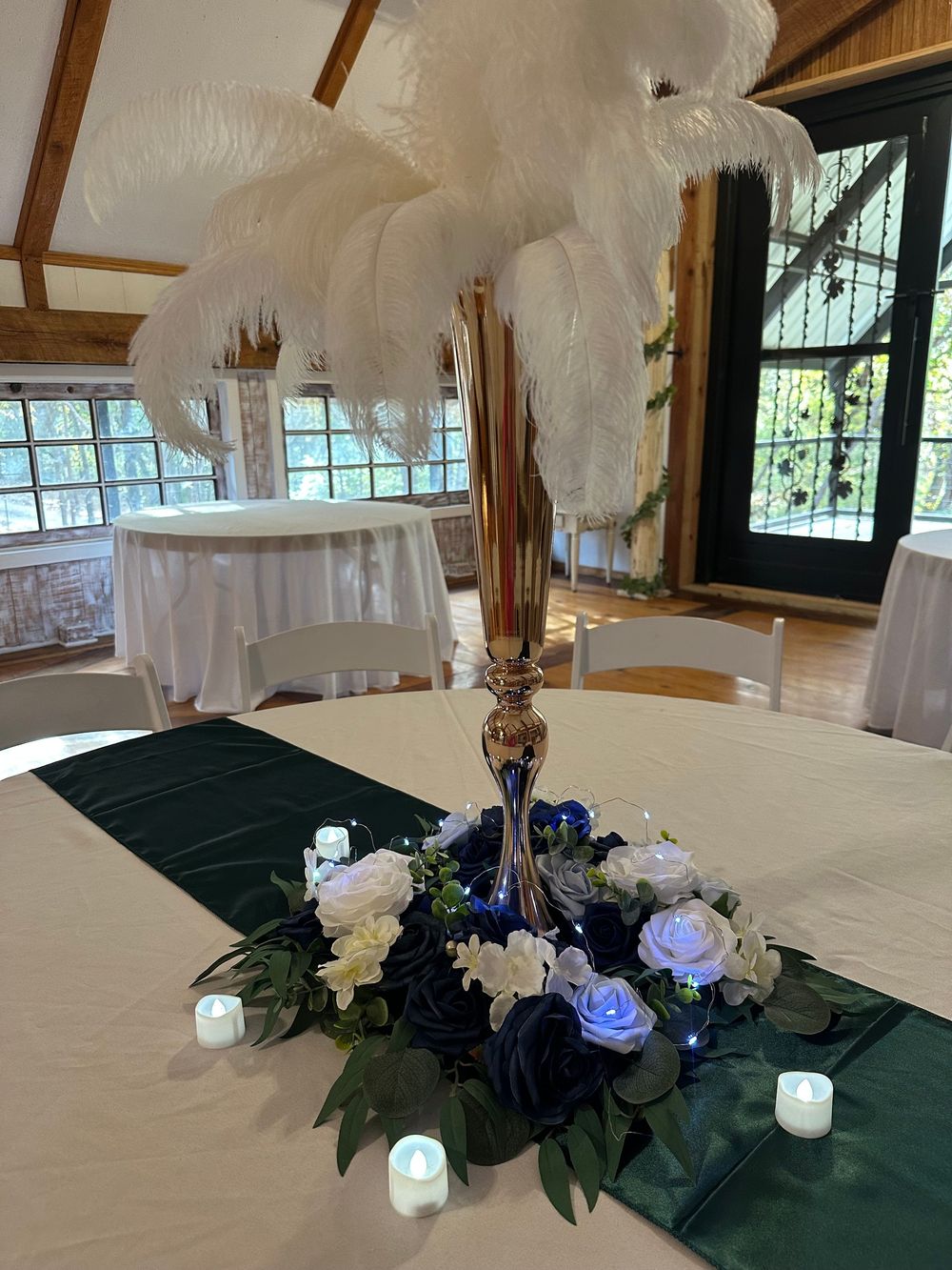 White feather centerpieces with blue roses and LED candles create an elegant table setting at a reception venue.
