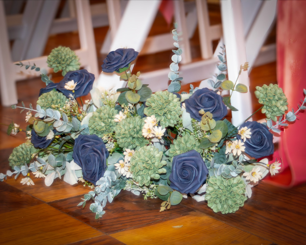 Blue roses and green succulent floral arrangement displayed against wooden table surface.
