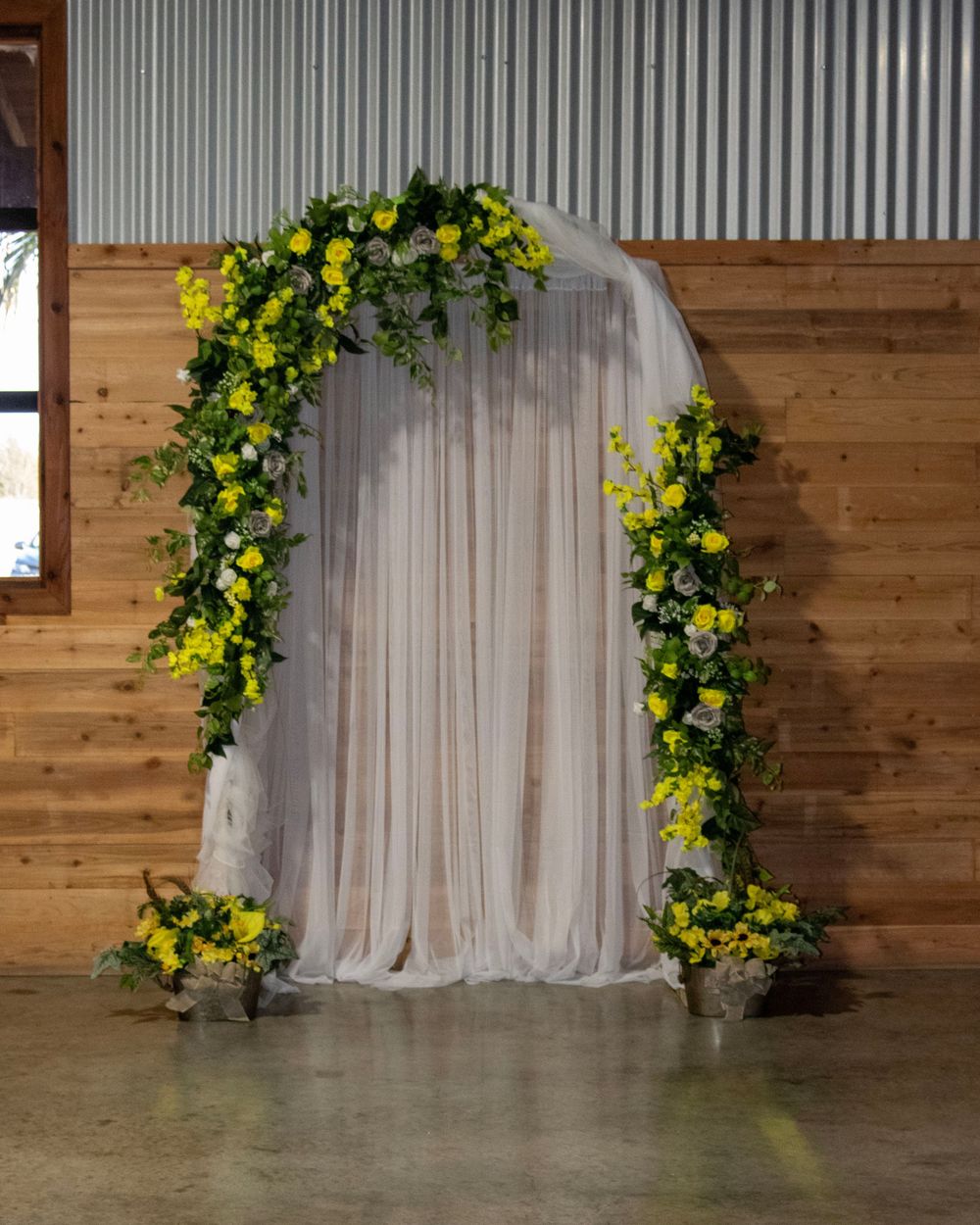 A rustic barn-style venue interior with white curtains and yellow floral arch decorations against wooden walls.
