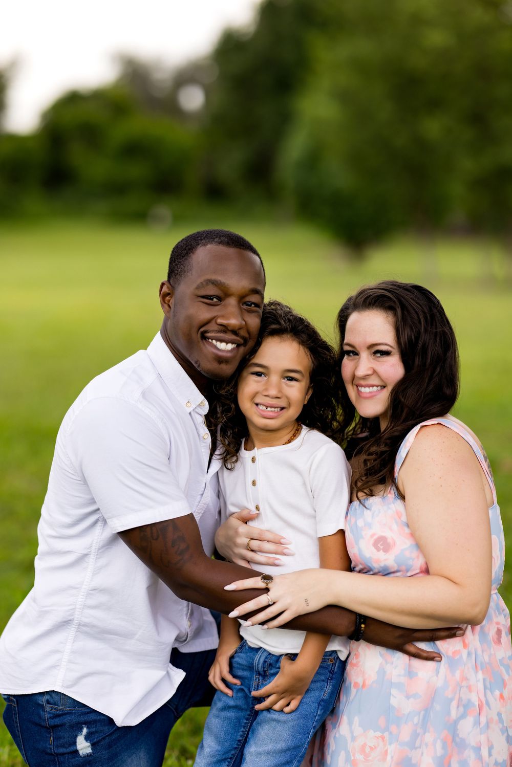 A family shares joyful embraces and laughter together during an outdoor photoshoot on a green lawn.