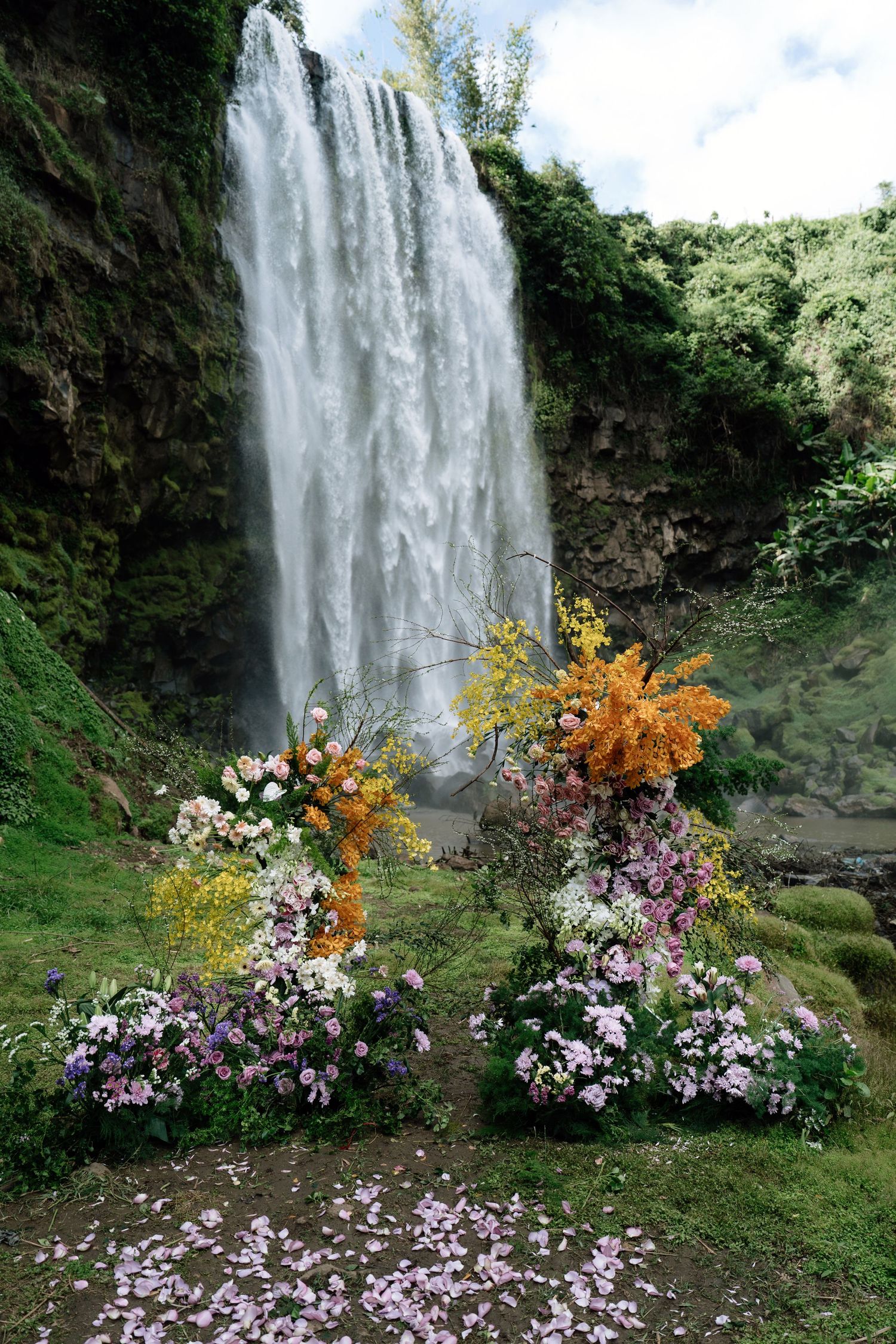 Colorful floral wedding arch arrangement set before a majestic cascading waterfall.