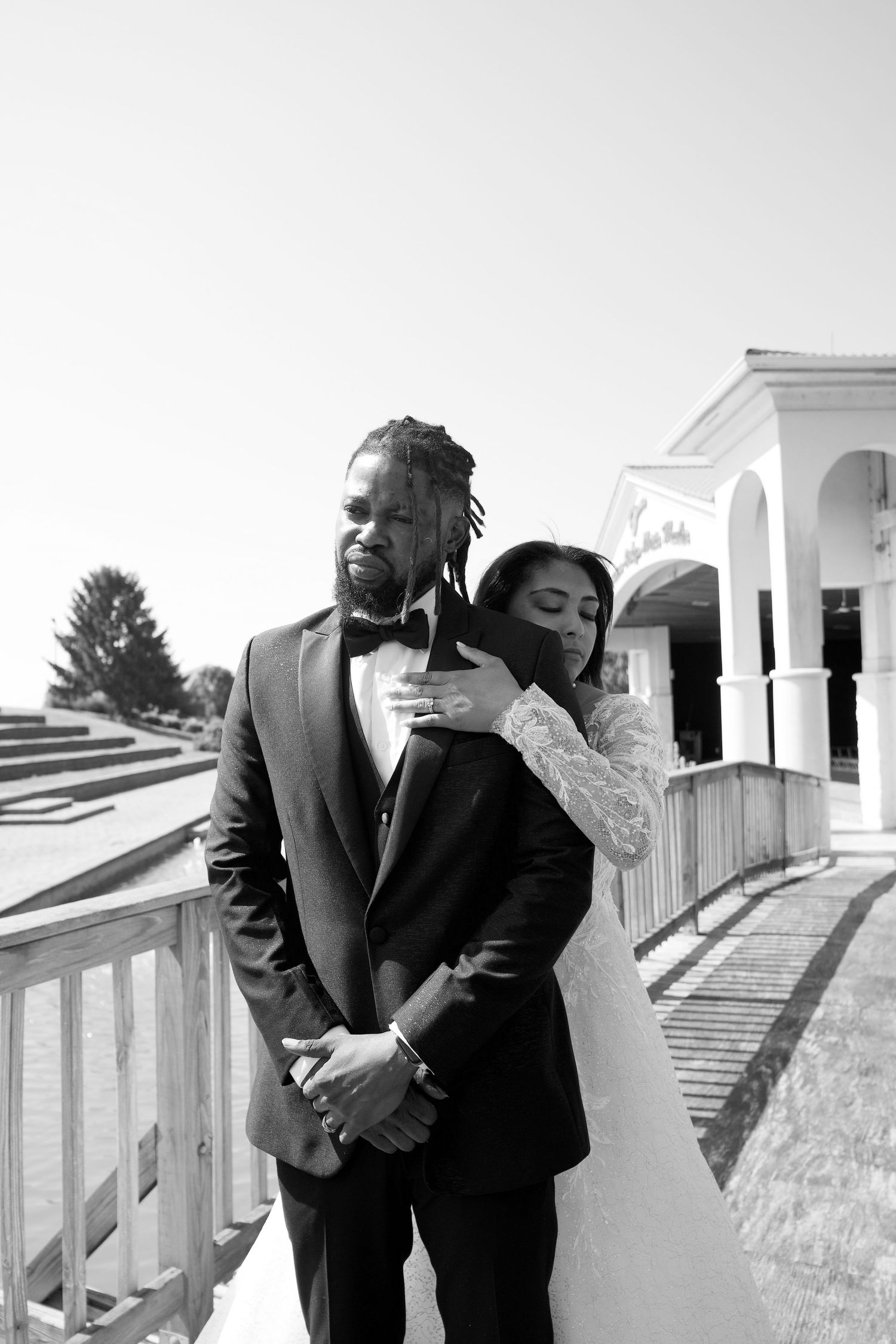 A black and white wedding portrait of a couple embracing on a white porch.