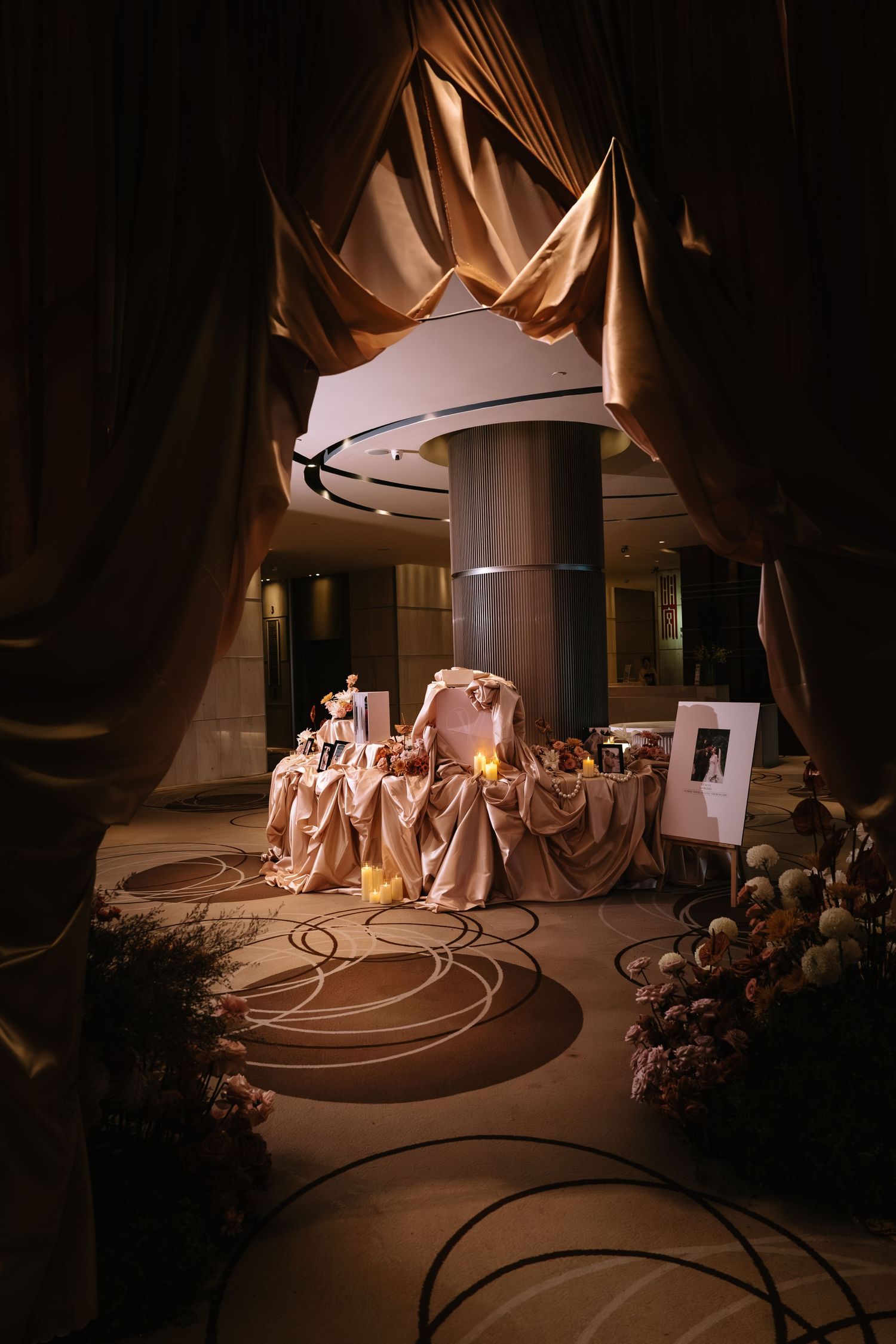Luxurious wedding reception hall with golden draped curtains, decorated sweetheart table, and ambient lighting.