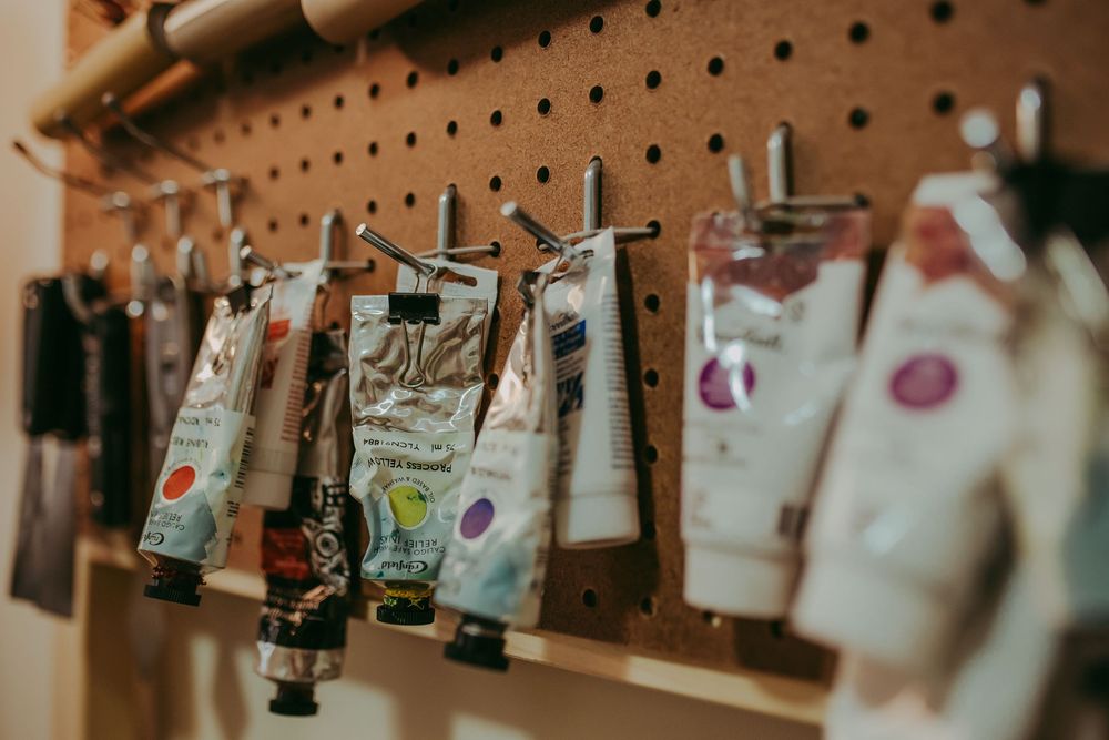 Artist paints are hung on display with wooden clothespins against a rustic wooden background. Small branding photography
