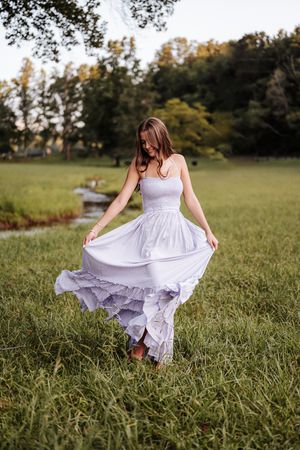 A person in a flowing white sundress twirls gracefully in a sunlit meadow during golden hour.
