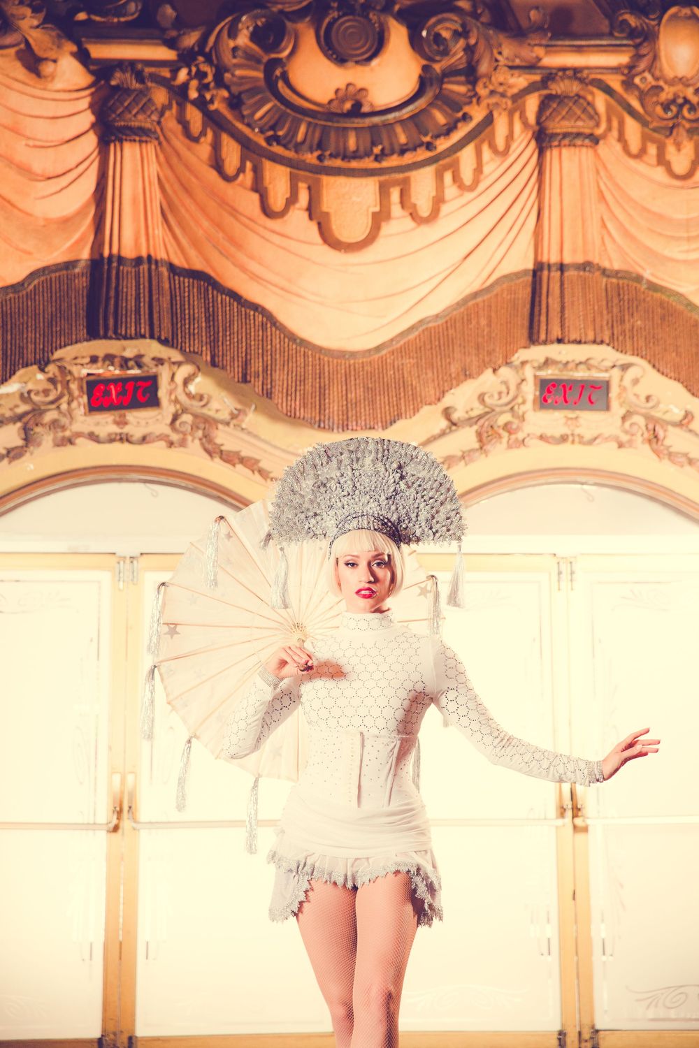 Performer in white sequined costume and dramatic headdress poses on ornate stage.