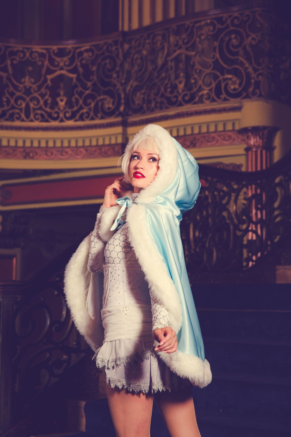 Dramatic portrait featuring a white fur-trimmed hooded cape in an ornate vintage theater setting.