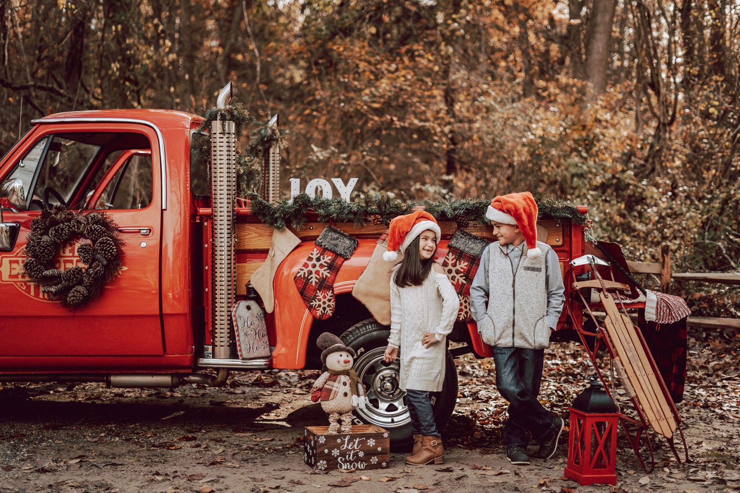 Kids posing in front of a vintage red truck with holiday decorations being photographed by Roots and Memories Family Photography Studio