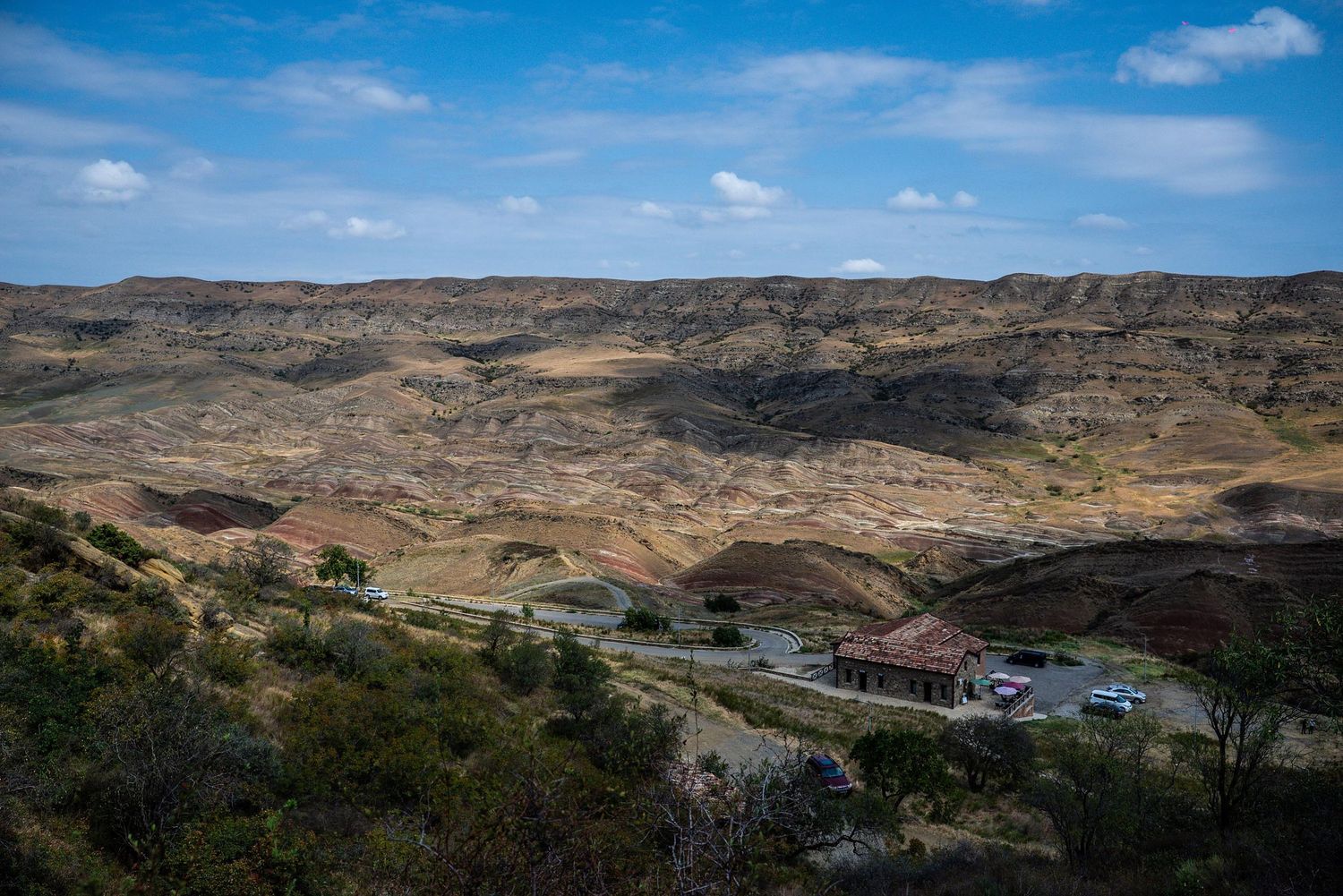 A scenic drive through winding mountain roads showcases rugged desert terrain and distant hills under blue skies.