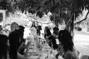 Groups of guests gather outdoors at an elegant garden party with tables and chairs under hanging decorations.