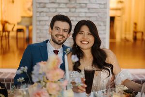Wedding reception setup in a brick-walled venue with warm lighting and floral centerpieces on tables.