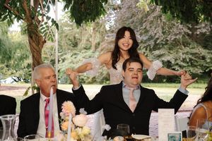 Wedding guests laugh and cheer during an outdoor celebration under natural greenery.