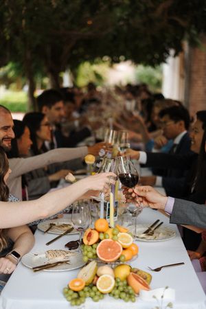 People toasting with wine glasses at an outdoor wedding reception table decorated with citrus fruits and place settings.