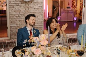Guests enjoying a wedding reception dinner at a table decorated with peach flowers and candles by a brick wall.