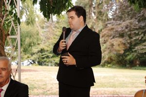 A person in black attire stands in profile against a blurred outdoor background during a fall day.