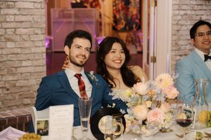Wedding guests seated at dining tables laughing and enjoying a reception celebration with wine glasses and floral centerpieces.