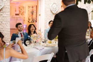 A couple dances together during their first dance at a wedding reception in a pink-lit venue with brick walls.