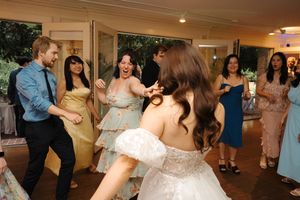 A group of people dancing and celebrating at an indoor wedding reception event.