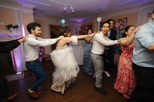 Wedding guests dancing energetically in a banquet hall with purple lighting and creating an enthusiastic party atmosphere.
