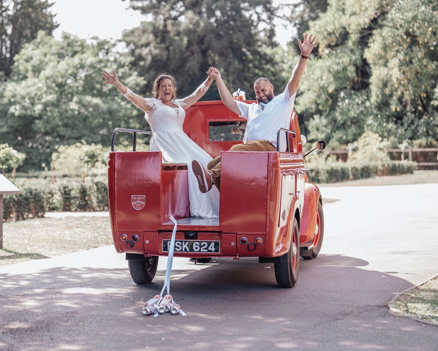 Vintage red pickup truck with people celebrating their wedding in the back on a sunny day.