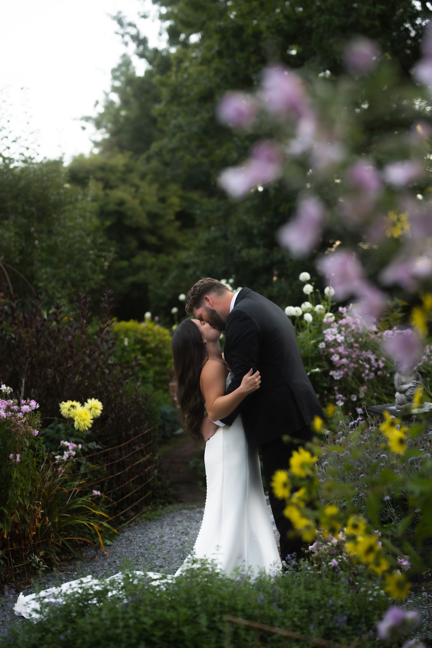 A couple shares an intimate moment in a romantic garden setting surrounded by purple and yellow wildflowers.
