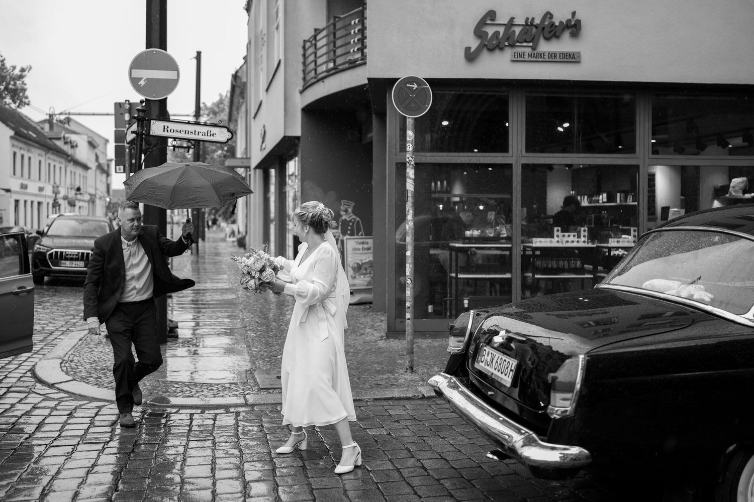 Hochzeitsfotograf Köpenick Berlin – Braut bekommt Blumen unter Regenschirm vor dem Standesamt Schwarz-Weiß