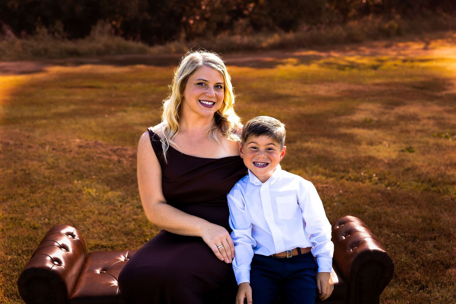 A family photo session at sunset in a grassy field with warm orange lighting and casual attire.