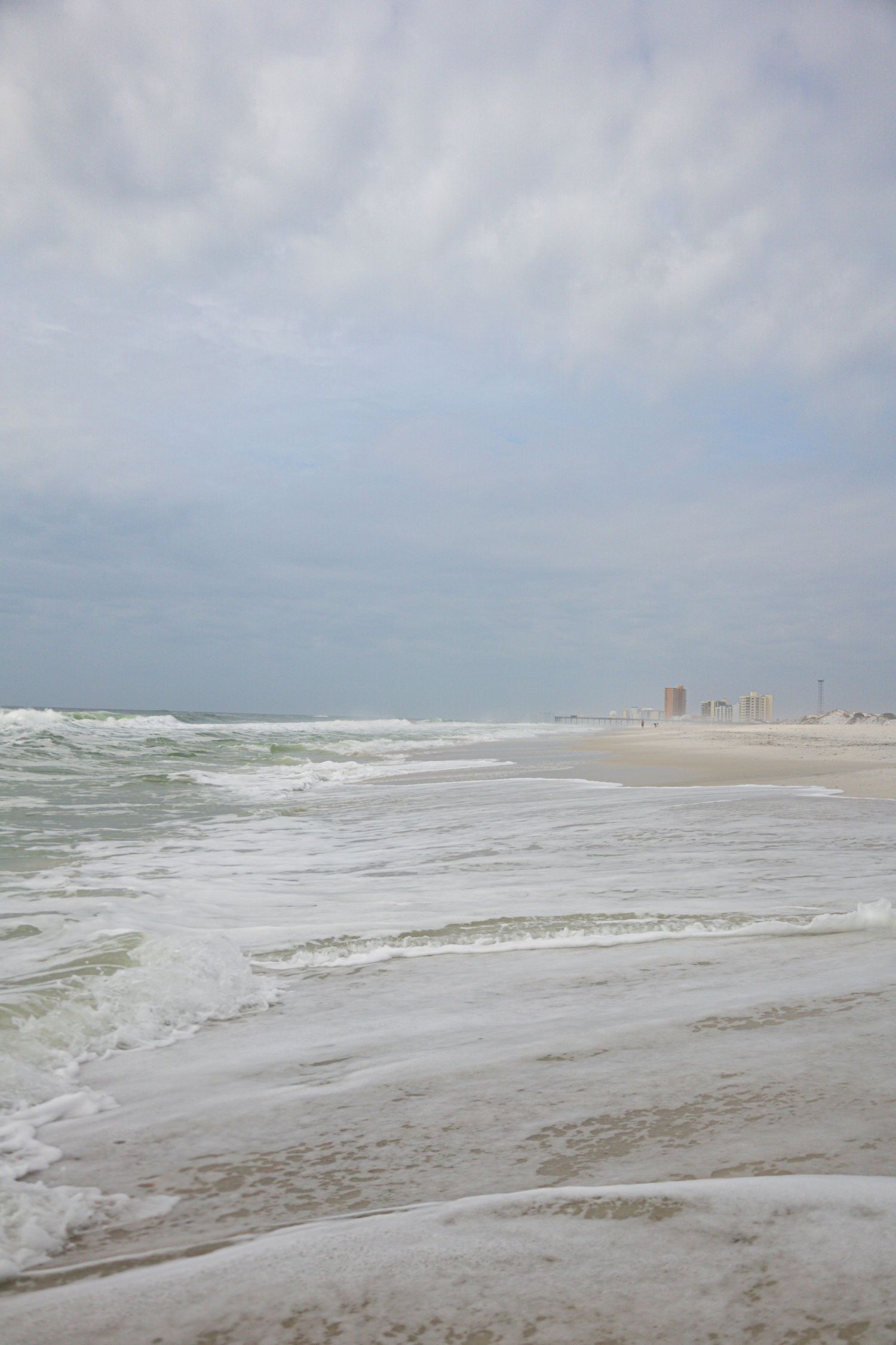 Stormy beach scene with crashing waves and overcast skies along the coastline.