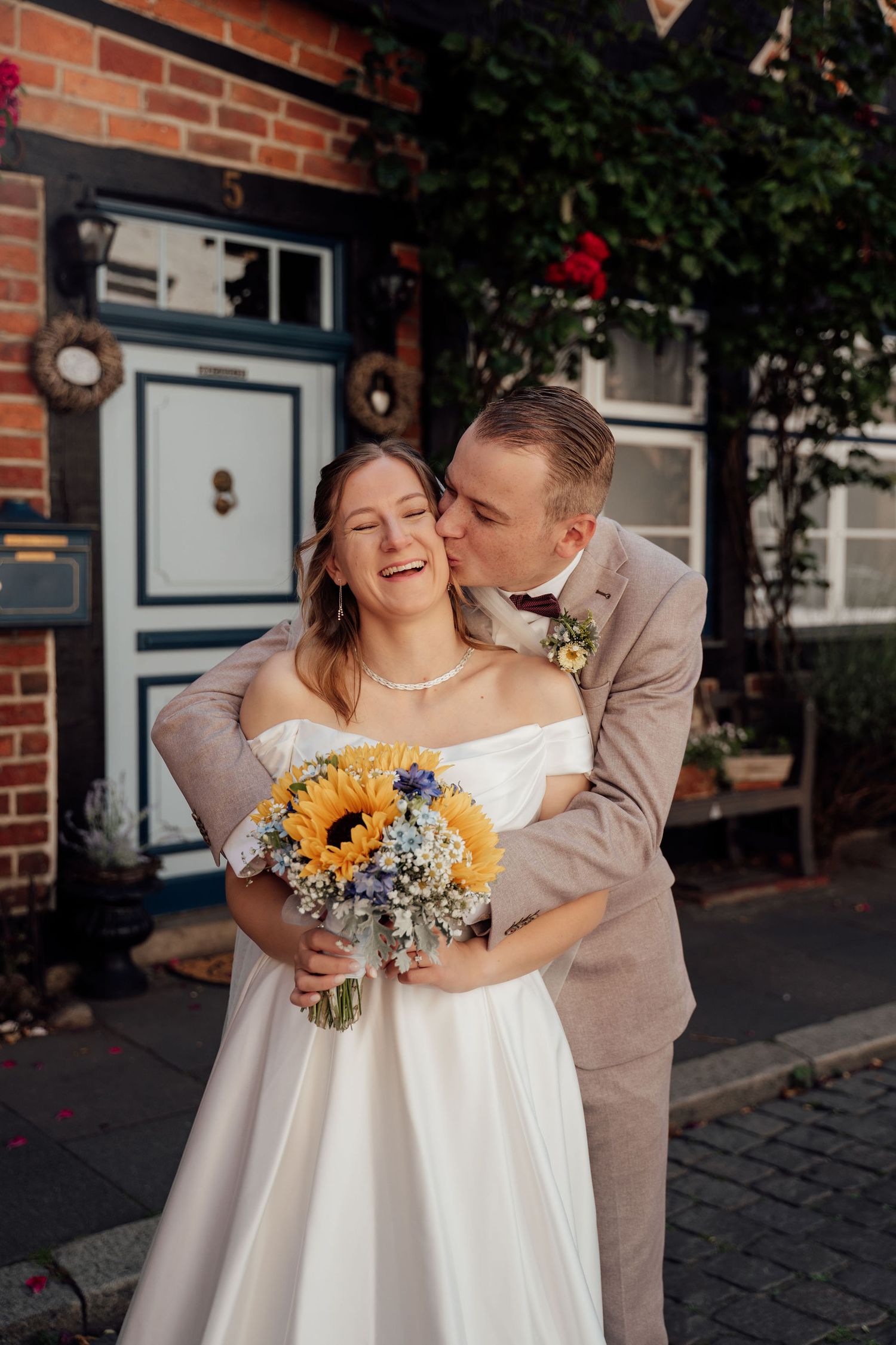 A romantic wedding moment captured outside a brick building with sunflowers in the bridal bouquet.