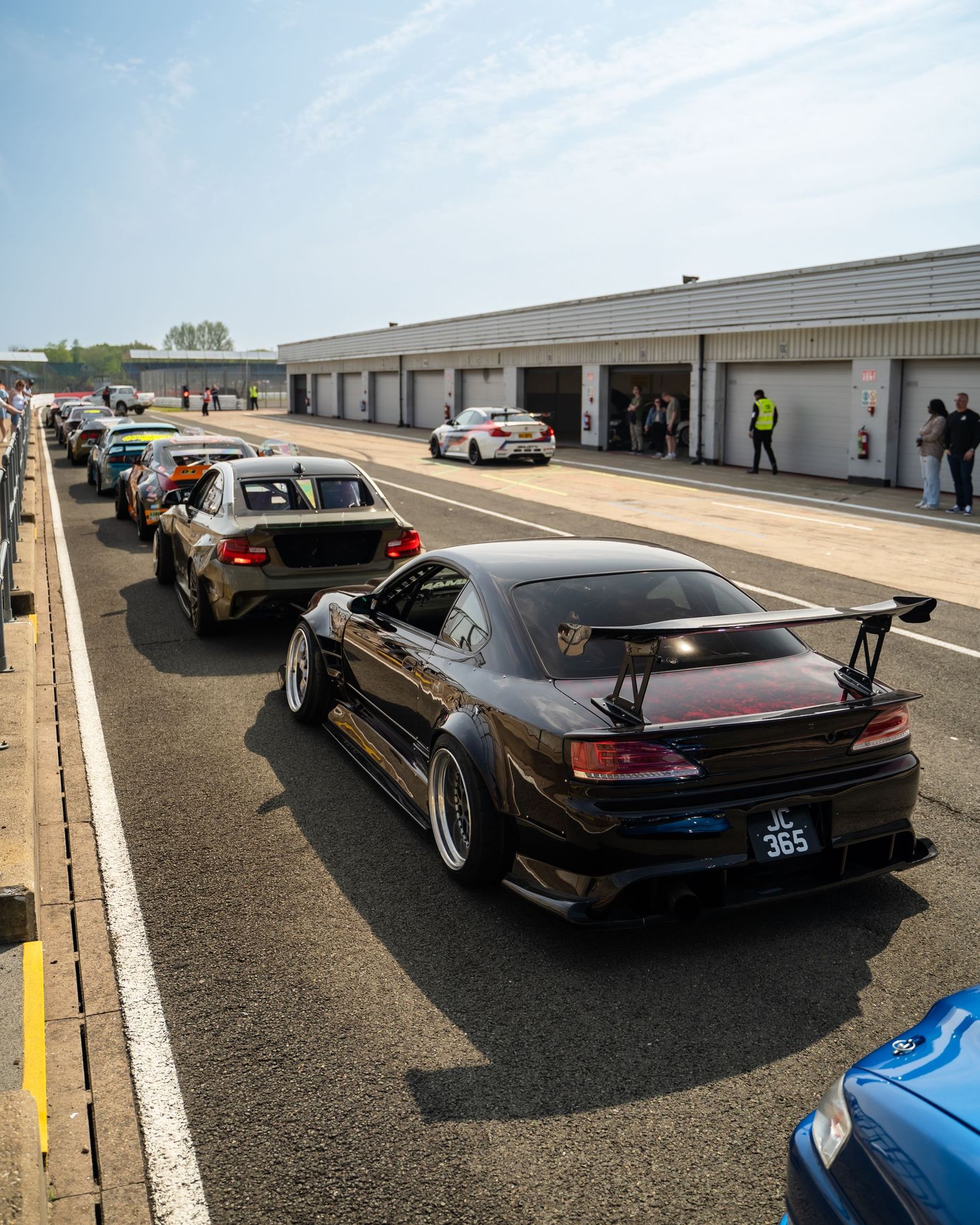 Modified black sports cars lined up in pit lane at a race track.