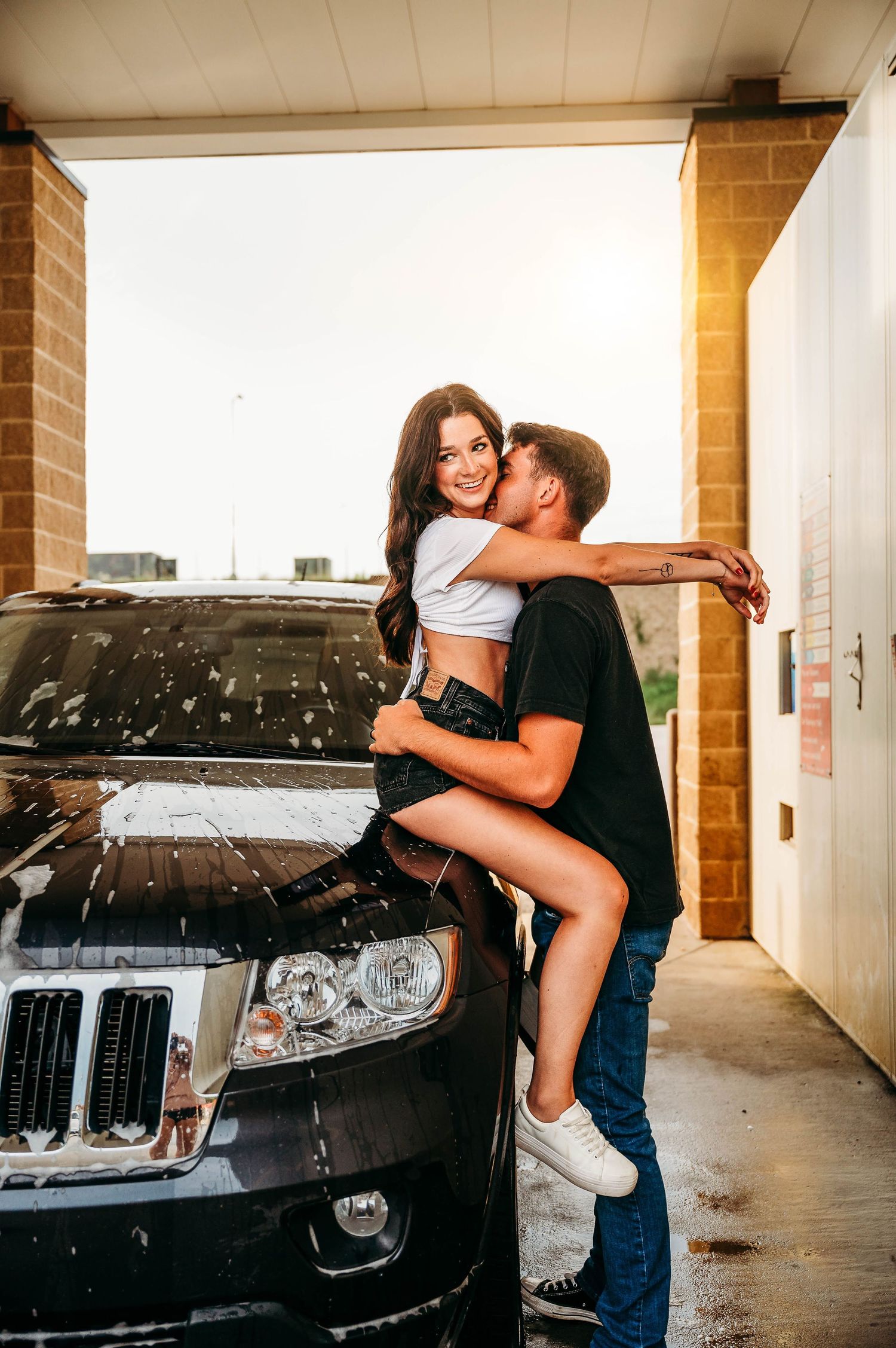 A couple embracing by a vintage car in an automotive service garage with moody lighting and industrial setting.