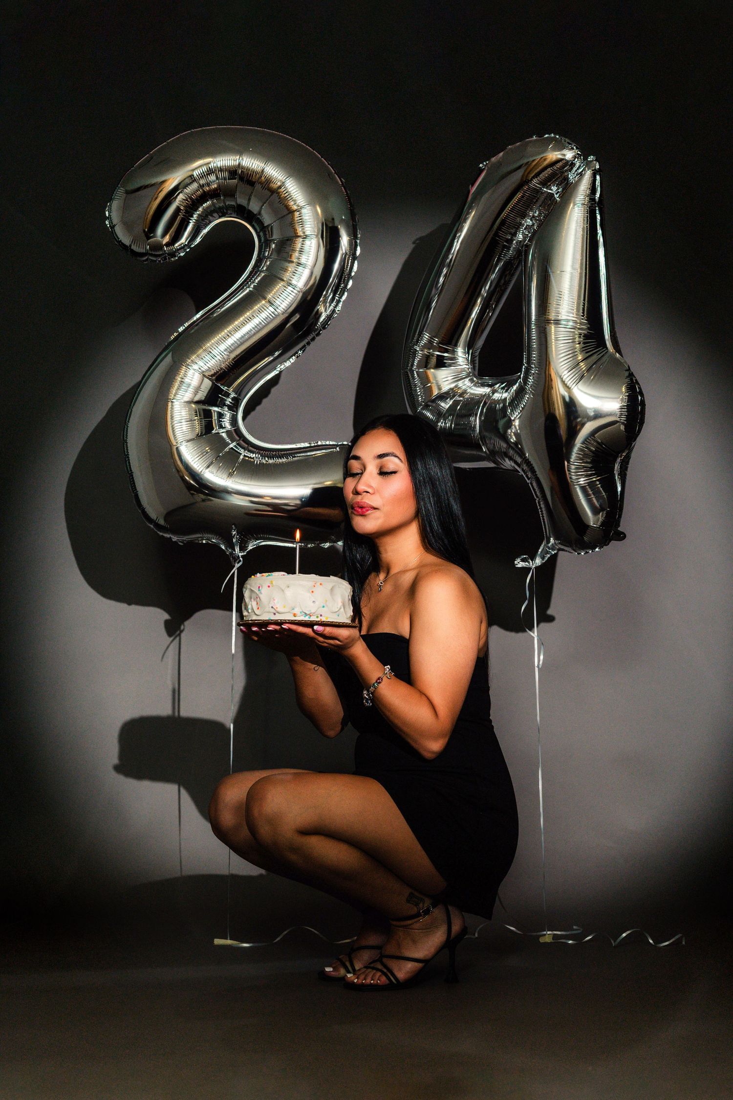 A silhouetted figure in black poses with silver number balloons against a dark background.