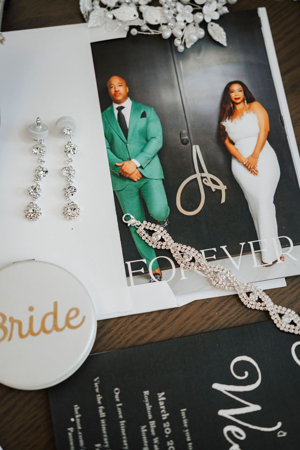 Wedding detail flatlay featuring jewelry, photos and decorative bride accessories on dark wood.