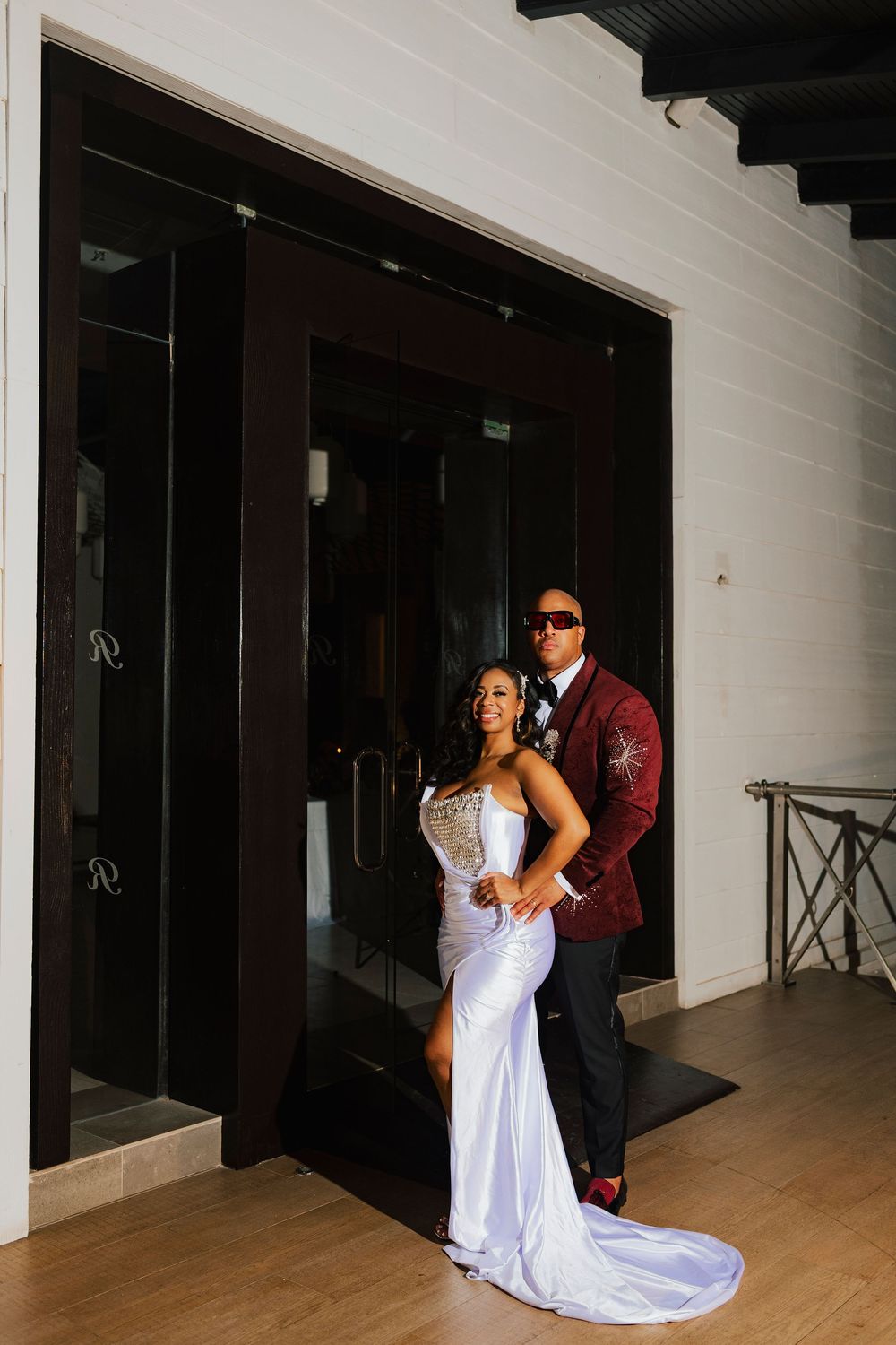 Elegantly posed couple in formal attire create dramatic silhouetted shots in a white hallway interior.