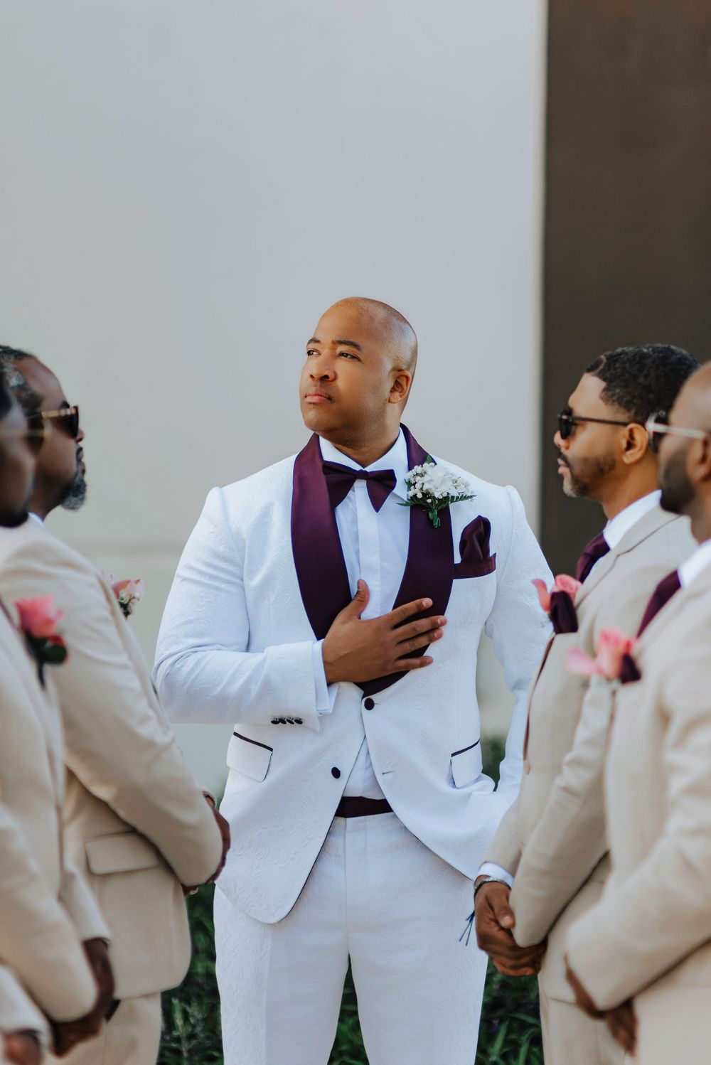 Groomsmen in crisp white tuxedos with burgundy accents standing together on wedding day.
