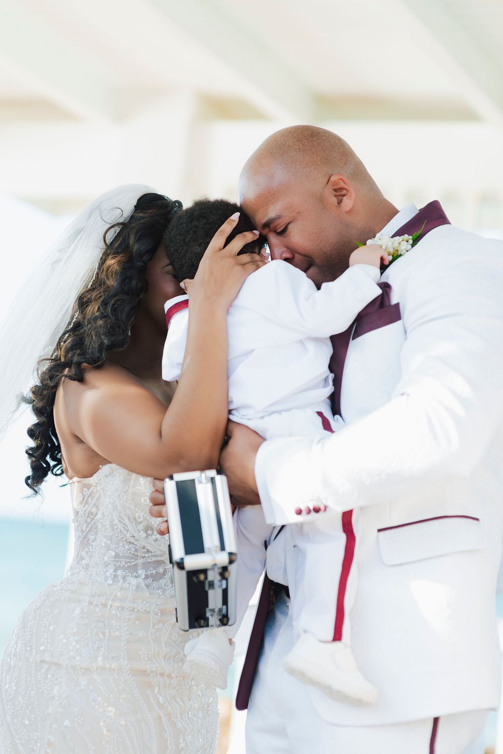Romantic wedding couple shares their first kiss in elegant white attire with burgundy accents.