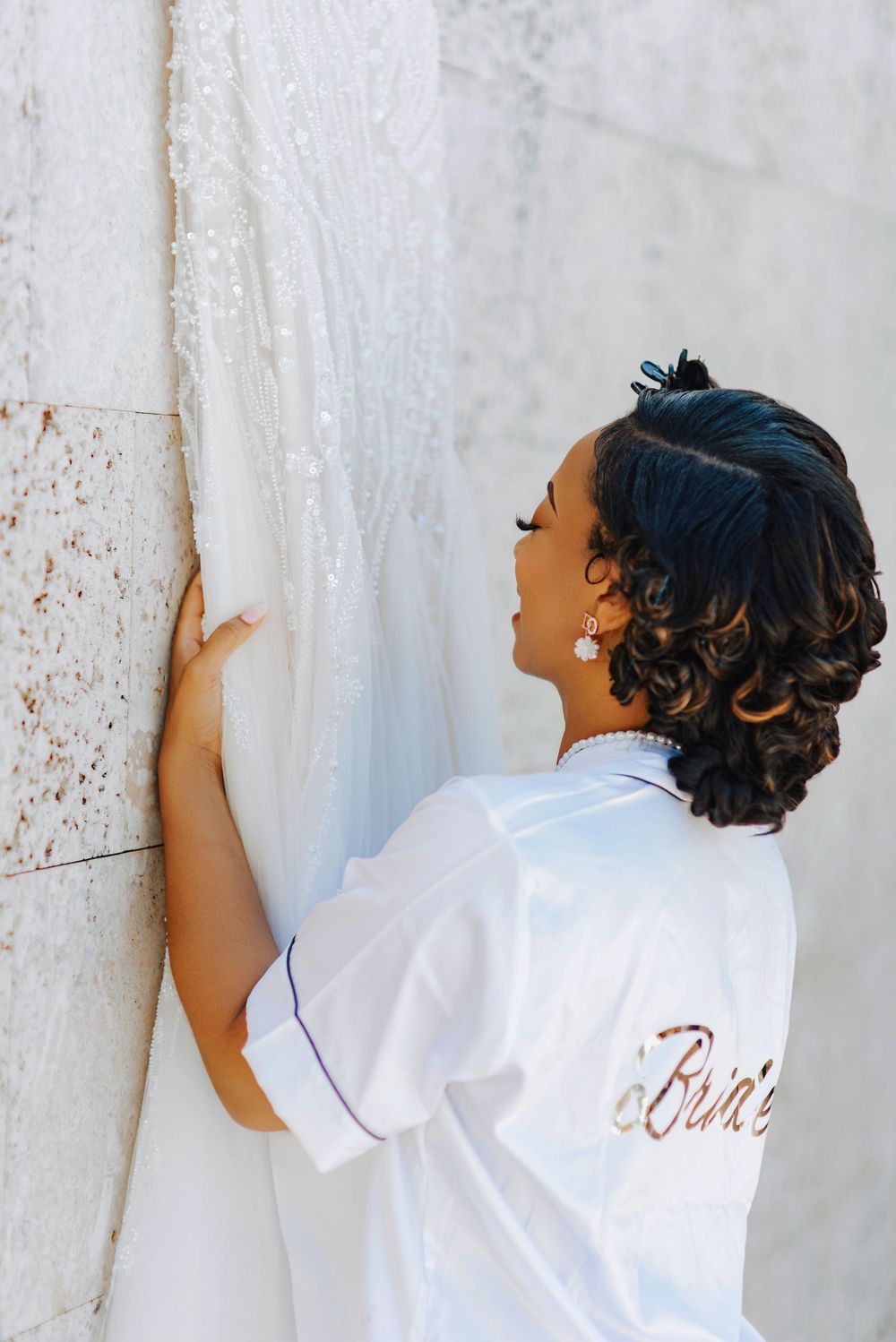 Bride wearing white robe poses against textured wall in artistic sequence.