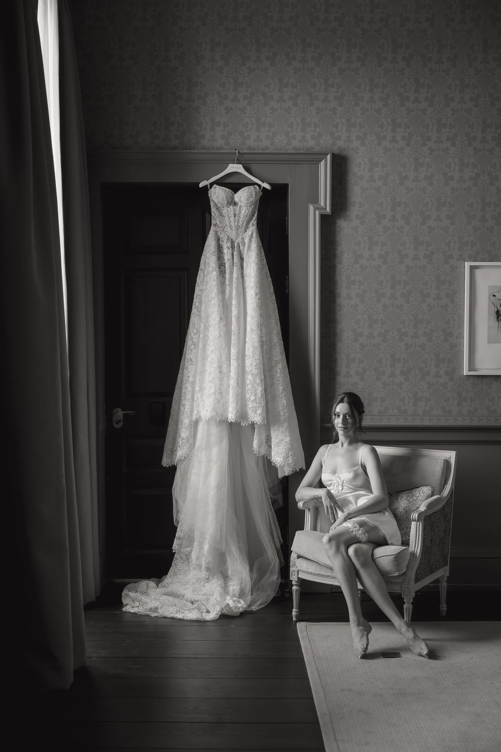 Wedding dress hangs elegantly in preparation room with antique furniture.