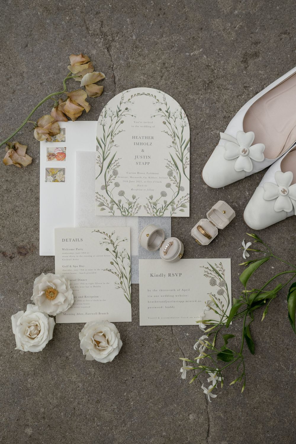 Elegant wedding invitation suite with delicate green botanical designs and white roses on textured gray background.
