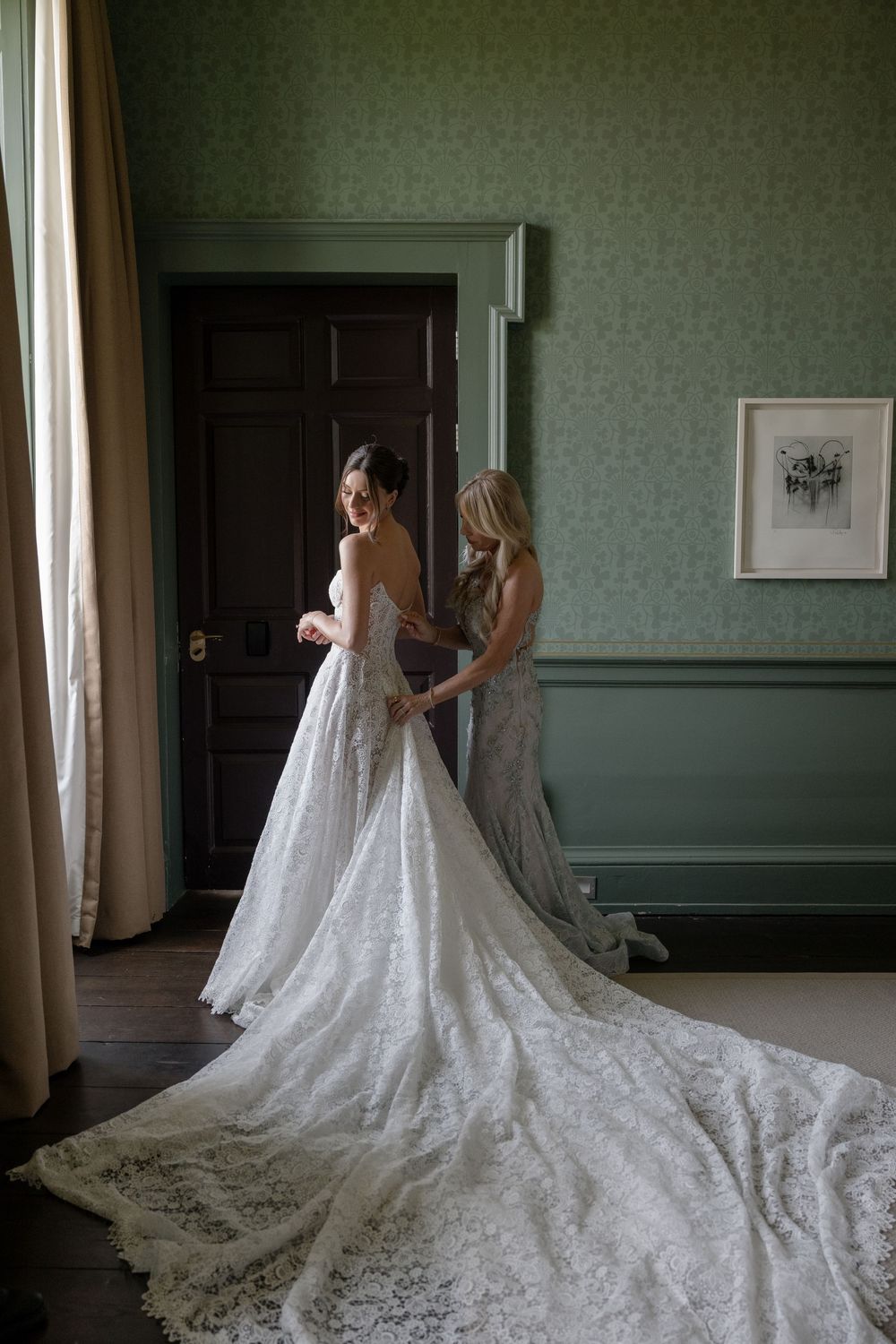 Elegant white lace wedding gown with cathedral train displayed in a grand room with mint green walls.