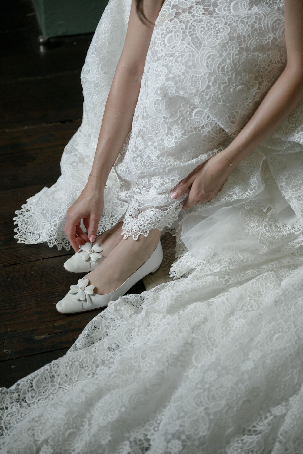 Detail shots of a bride putting on white wedding shoes with her lace dress.