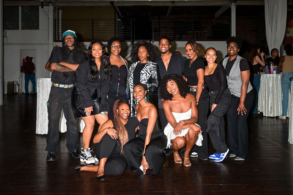Group photo of people wearing coordinated black and white outfits posing together at an indoor event space.